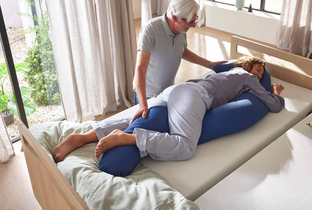 Frau wird von einem Pfleger mit dem Full Body Positionierungskissen in der Bauchlage positioniert