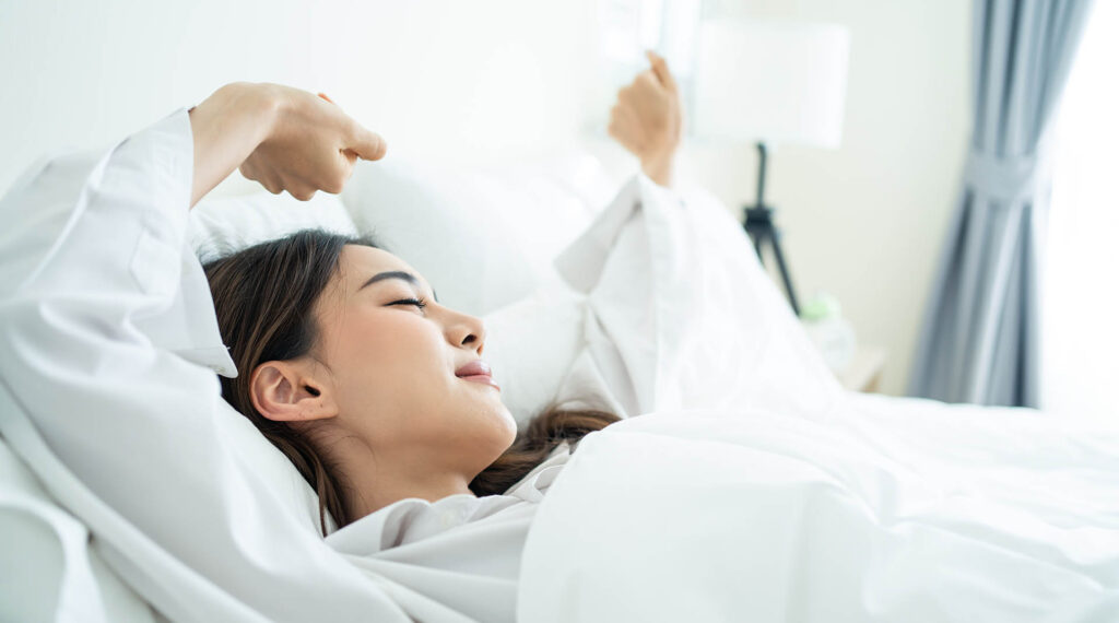 Junge Frau liegt im Bett und streckt sich