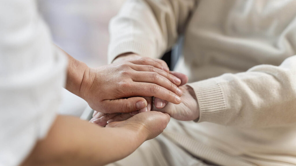 Pflegerin legt ihre Hände auf die des Patienten